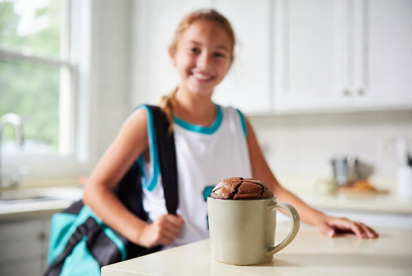 A teen athlete in a bright kitchen after practice with a chocolate protein mug cake on the counter.
