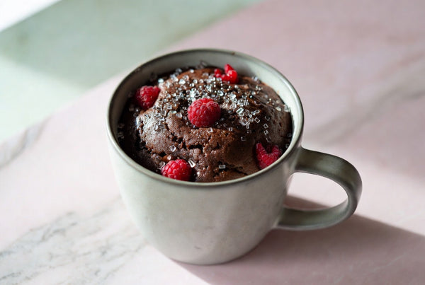 A warm chocolate protein mug cake topped with raspberries and sparkling sugar crystals in a ceramic mug.