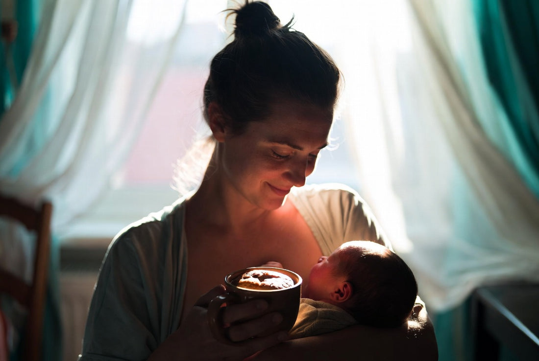 A new mother cradling her baby while holding a warm protein mug cake in soft morning light.